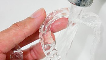 Patient rinsing clear aligner with water in sink