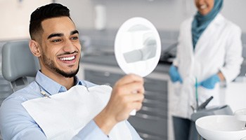 Man smiling at reflection in handheld mirror